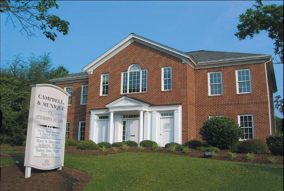 The offices of Campbell & Munique, a two-storey red brick building with a white columned entrance, set back behind a lawn with the firm's sign at the roadside
